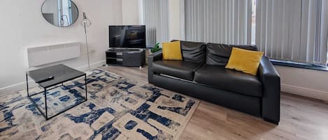 A modern living room with a black leather sofa, a small black table, a large mirror, and a TV.