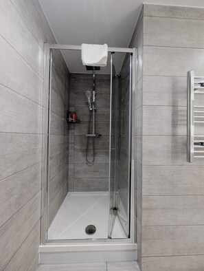 Une cabine de douche fermée par des parois en verre, avec une serviette blanche suspendue à un porte-serviettes, une douchette à main et un robinet fixé au mur.
