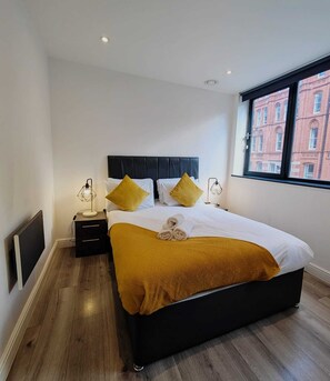 Une chambre d’hôtel avec un grand lit, une fenêtre donnant sur la ville, une table de chevet avec une lampe et un plancher en bois.