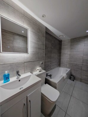 Ein modernes Badezimmer mit einem großen Spiegel, zwei Waschbecken, einer Badewanne und einer Toilette.