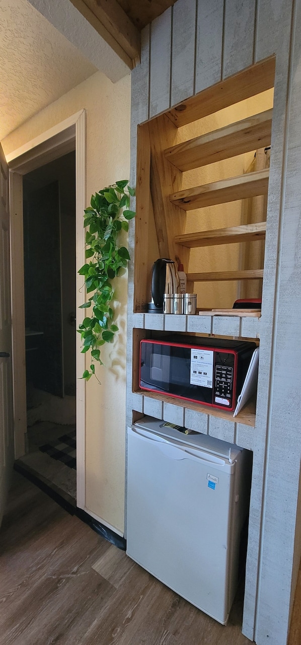 A compact kitchen with built-in appliances, a wooden shelf, and a potted plant.