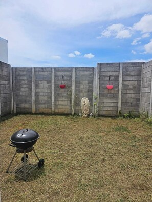 Ein Garten mit Grill, Statue und zwei roten, hängenden Pflanzgefäßen.