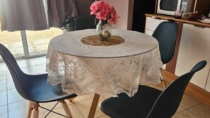 Zona pranzo con tavolo apparecchiato per due, un vaso con fiori e angolo cottura con microonde e frigorifero.
