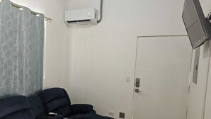 Una stanza con un divano blu scuro, un condizionatore d'aria, una televisione a parete e una porta.
