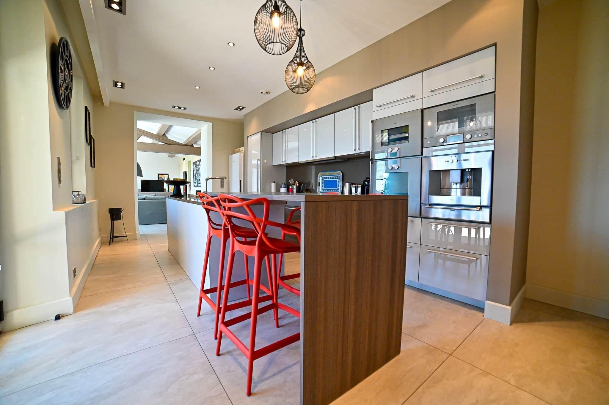 A modern kitchen with stainless steel appliances, a wooden island, and red bar stools.