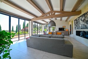 Ein großzügiger Wohnraum mit einem großen grauen Sofa, einem Fernseher und einem Essbereich mit Tisch und Stühlen.