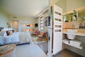 Una camera da letto moderna con un letto, comodini, una sedia, un divano e un bagno con lavandino e specchio.