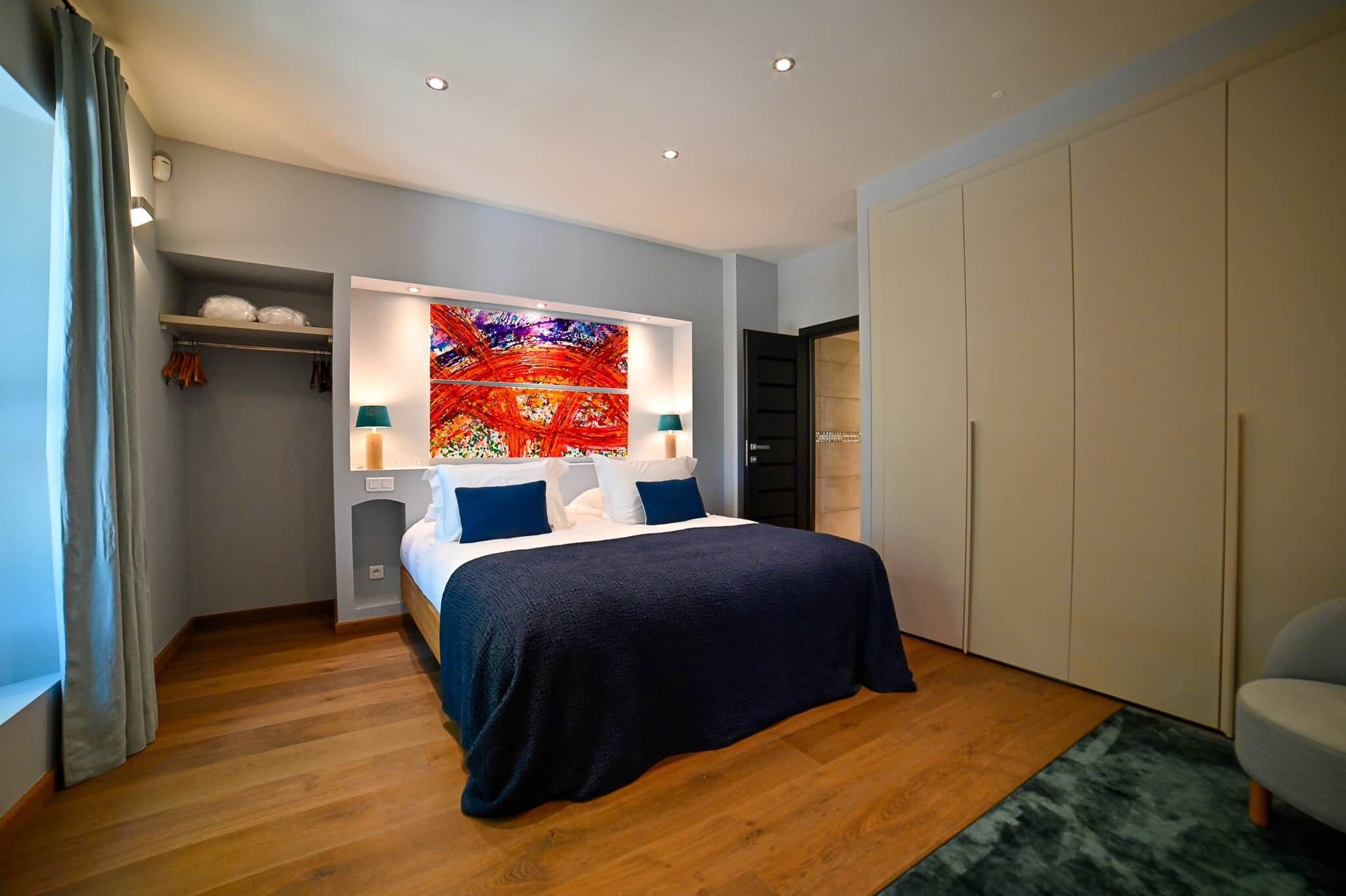Une chambre à coucher moderne avec un grand lit, une armoire et un tableau abstrait aux couleurs vives accroché au mur.
