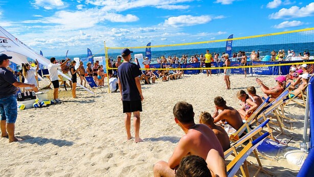 En strandvolleybollmatch med åskådare och spelare på en sandplan.