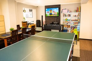 Een kamer met een pingpongtafel, een tafelvoetbaltafel, een televisie en een boekenkast vol speelgoed.