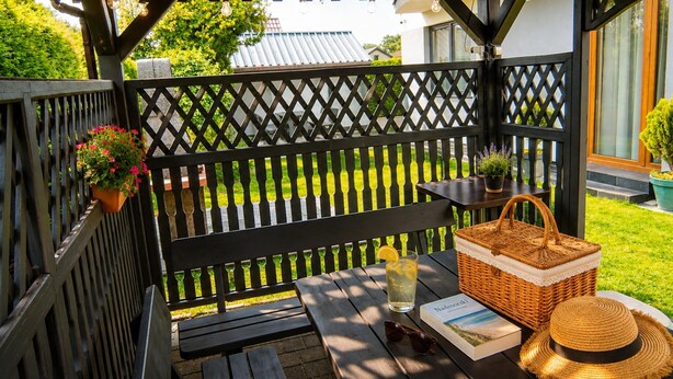 En træterrasse med en bænk, et bord med en drik, en kurv og en bog.