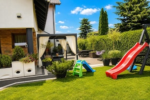 Ein Wohnbereich im Freien mit Terrasse, Sitzgelegenheiten, einer Rutsche und einem Pergola.