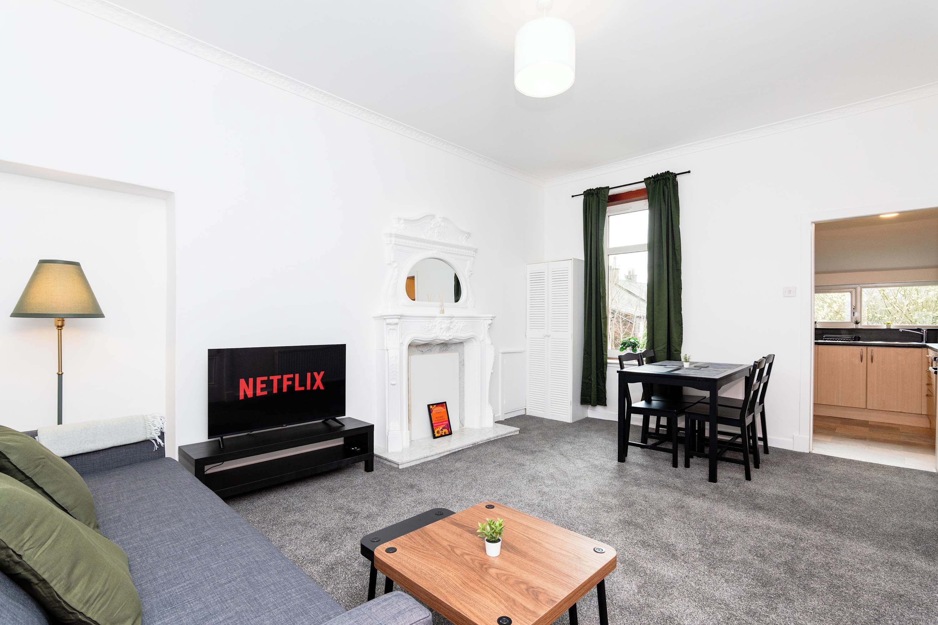 Una sala de estar moderna con un televisor de pantalla plana, chimenea, comedor y una cocina visible a través de un acceso abierto.