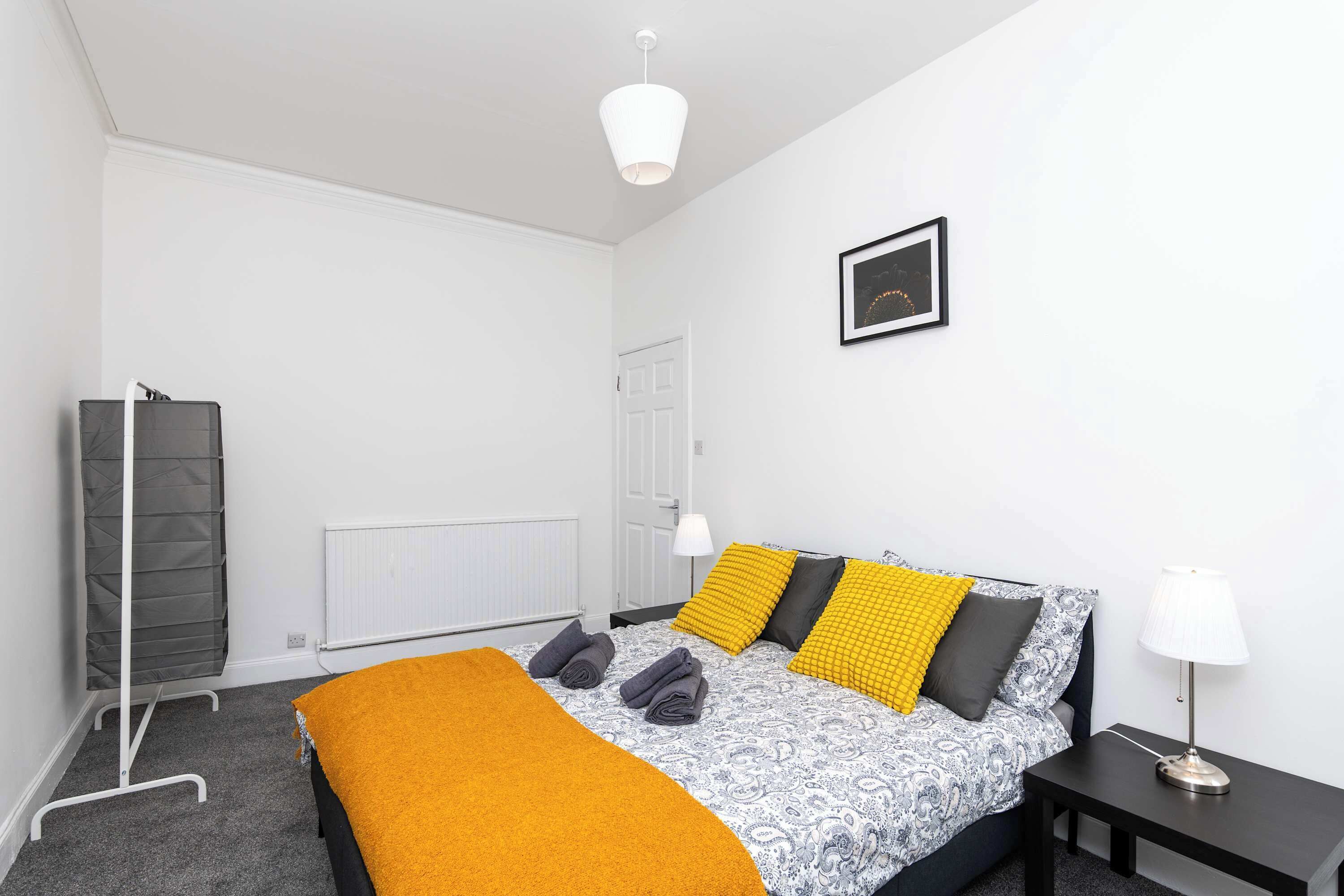 Une chambre à coucher avec un lit, des tables de chevet, un radiateur, un porte-manteau et un tableau encadré au mur.