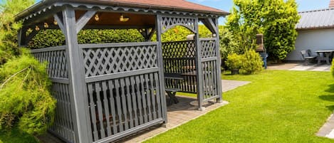 A gazebo with a lattice design, a tiled roof, and a surrounding lawn.