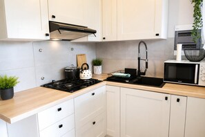 A modern kitchen with white cabinets, a gas stove, a kettle, a microwave, and a sink with a faucet. - Studio for 3 people, close to the sea (Dziwnówek)