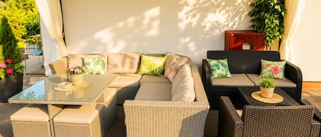 Un patio con mobiliario de mimbre, que incluye un sofá, dos sillones y una mesa de vidrio.