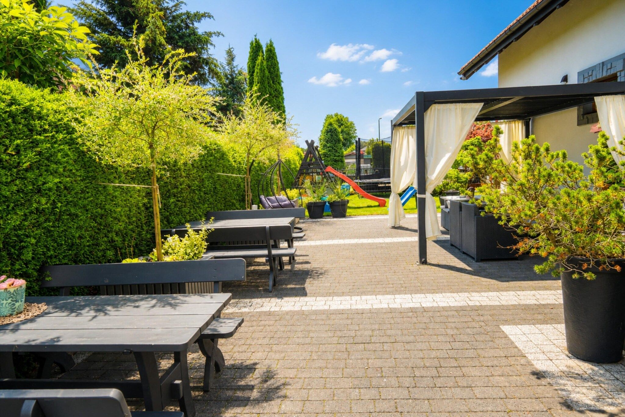 An outdoor patio area with multiple tables and benches, a children's play structure, and potted plants.