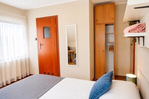 A bedroom with a bed, a wardrobe, a mirror, and a shelf with towels.