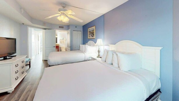 A hotel room with two beds, a television, a ceiling fan, and a door leading to a bathroom. - Carolinian Beach Resort 1731 (Myrtle Beach)