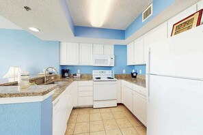 A kitchen with white cabinets, a microwave, a stove, and a refrigerator. - Carolinian Beach Resort 1731 (Myrtle Beach)