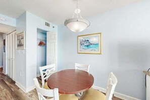 A dining area with a round table, white chairs, and a ceiling light fixture. - Carolinian Beach Resort 1731 (Myrtle Beach)
