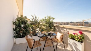 A balcony with a table set for two, wicker chairs, potted plants, and a city view. - ALL Gargasole | Luxury Sky-High Retreat with 2 Private Terraces (Bari)