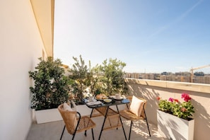 A balcony with a table set for two, wicker chairs, potted plants, and a city view. - ALL Gargasole | Luxury Sky-High Retreat with 2 Private Terraces (Bari)