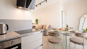 A modern kitchen with a built-in oven, a coffee maker, and a dining area with a glass table and cushioned chairs. - ALL Gargasole | Luxury Sky-High Retreat with 2 Private Terraces (Bari)
