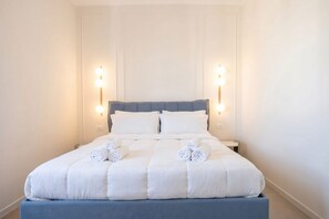 A neatly made bed with white bedding and rolled towels, a blue headboard, and wall-mounted lights on either side. - ALL Gargasole | Luxury Sky-High Retreat with 2 Private Terraces (Bari)