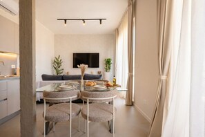 A modern dining area with a glass table, four upholstered chairs, a flat-screen TV mounted on the wall, and a sofa in the background. - ALL Gargasole | Luxury Sky-High Retreat with 2 Private Terraces (Bari)