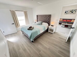 Une chambre à coucher moderne avec un grand lit, une table de chevet, une commode et un canapé dans la pièce adjacente.