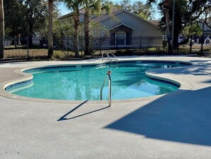 Une piscine à bord incurvé, entourée d’une terrasse dallée et d’une clôture en métal.