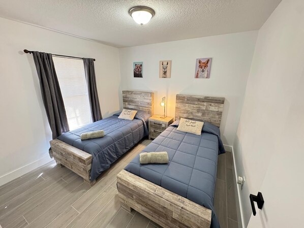 Une chambre avec deux lits, une fenêtre avec des rideaux et des œuvres d’art murales.