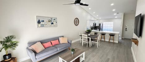 A modern living room with a grey sofa, a coffee table, and a dining area with a white table and chairs.