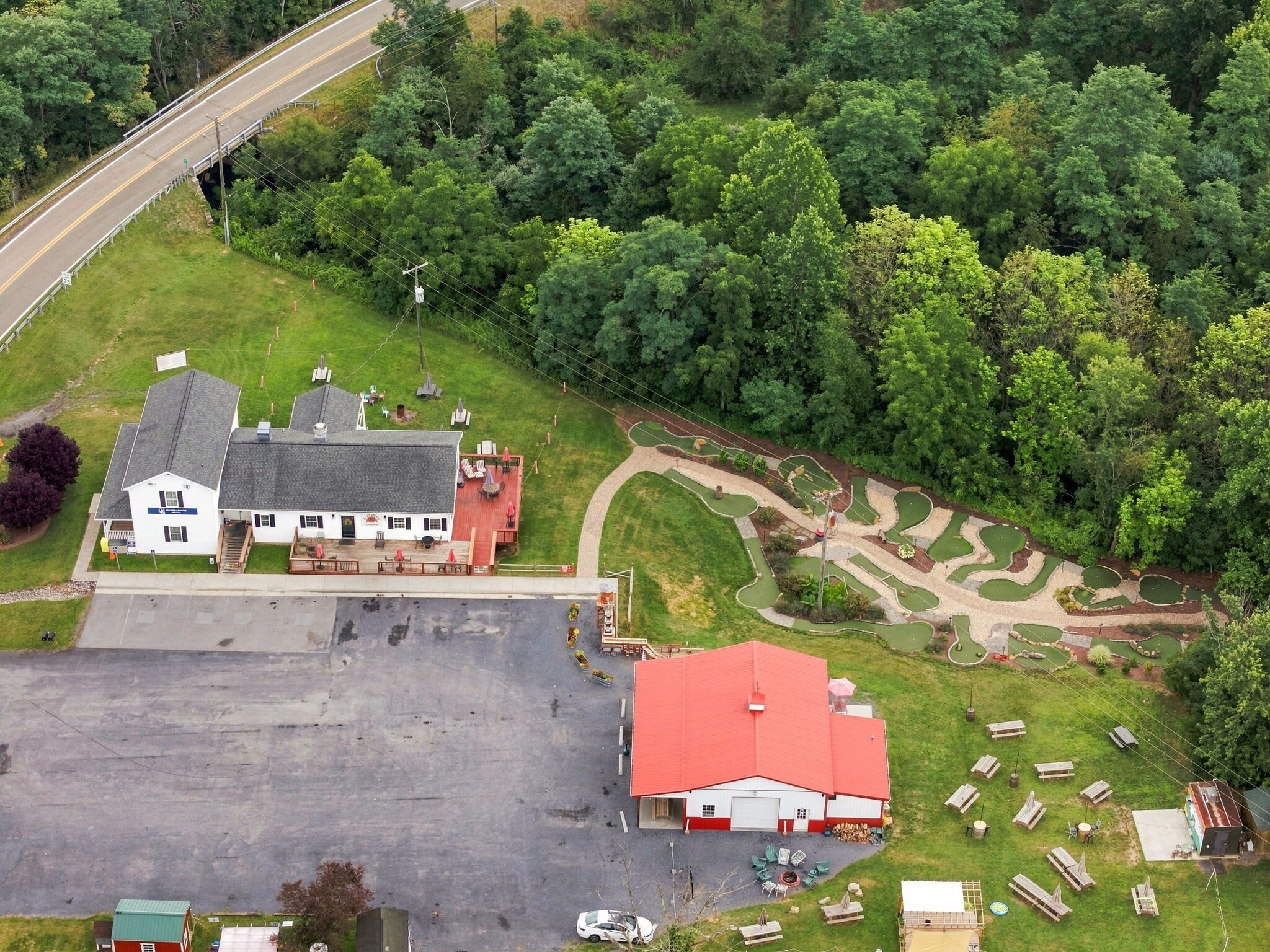 An aerial view of a property with a large parking lot, a red-roofed building, and a green lawn with a winding path.