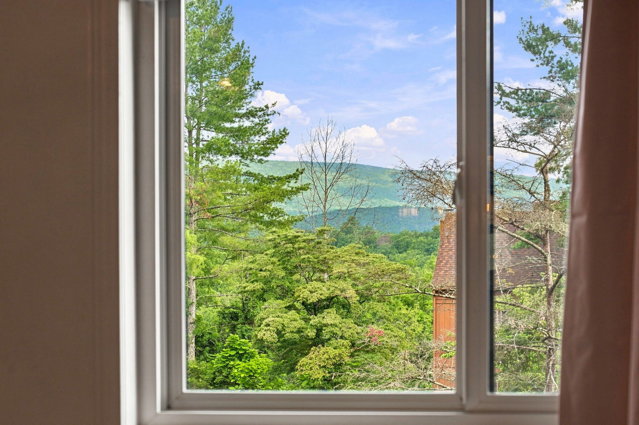 Uma janela com vista para uma paisagem arborizada e uma chaminé de tijolos.