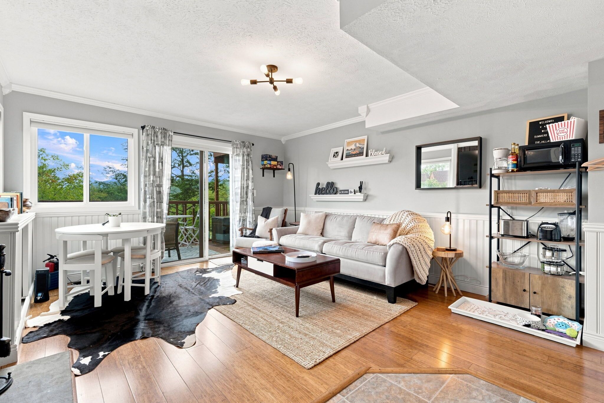 A spacious living room with a large window, a white sofa, a wooden coffee table, and a dining area with white chairs.