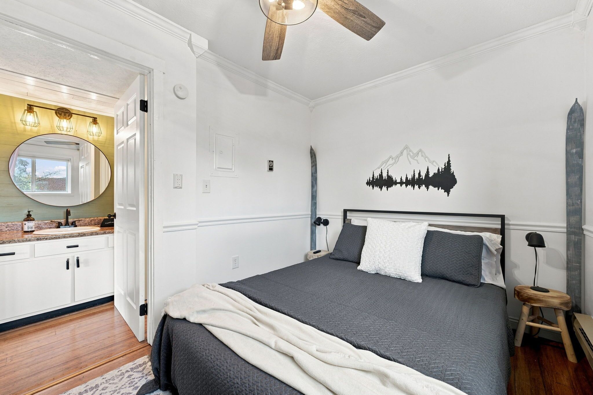 Une chambre à coucher comprenant un lit, une table de chevet, un miroir et un luminaire fixé au mur.