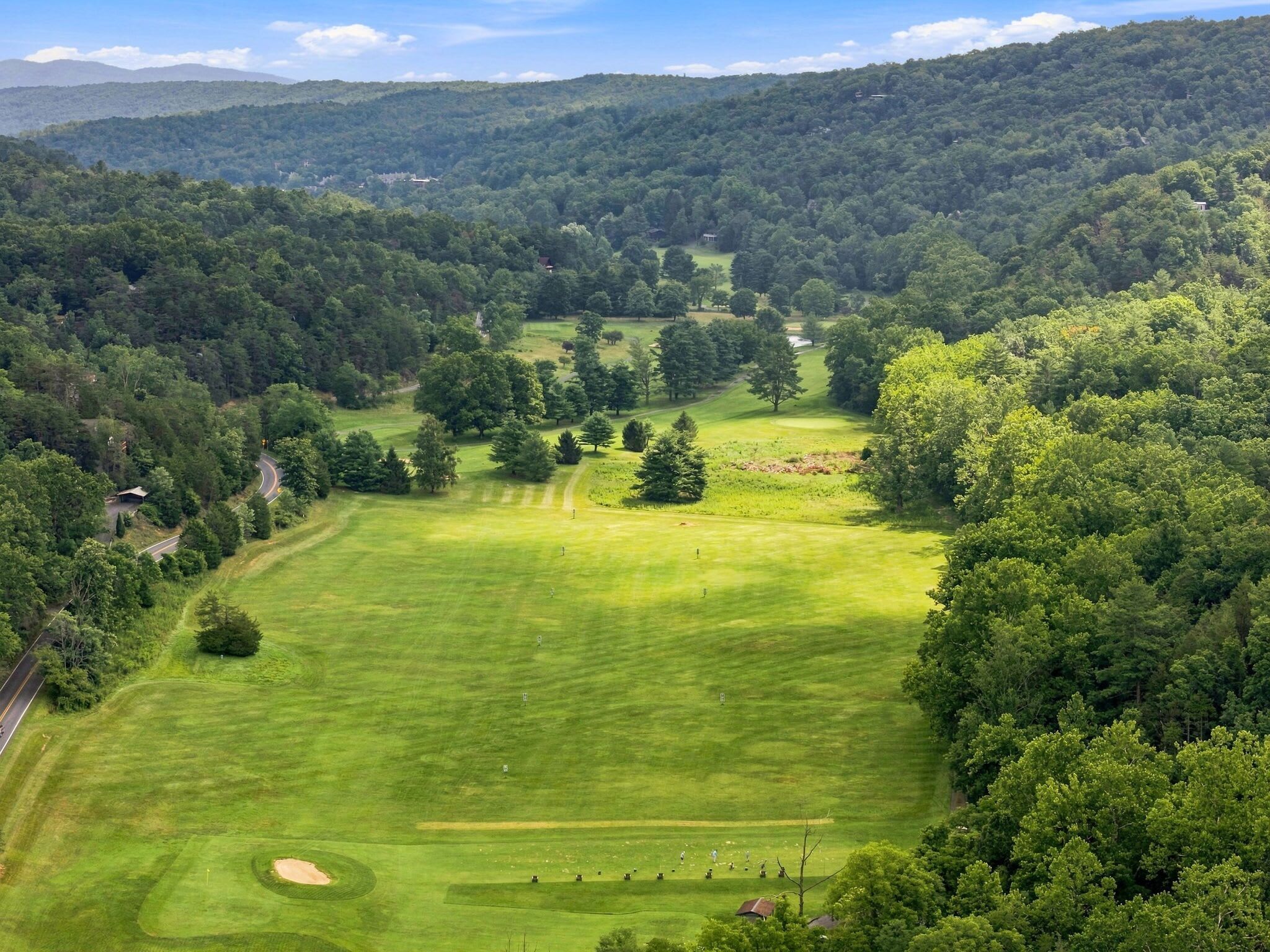 A golf course surrounded by dense forest with a clear sky.