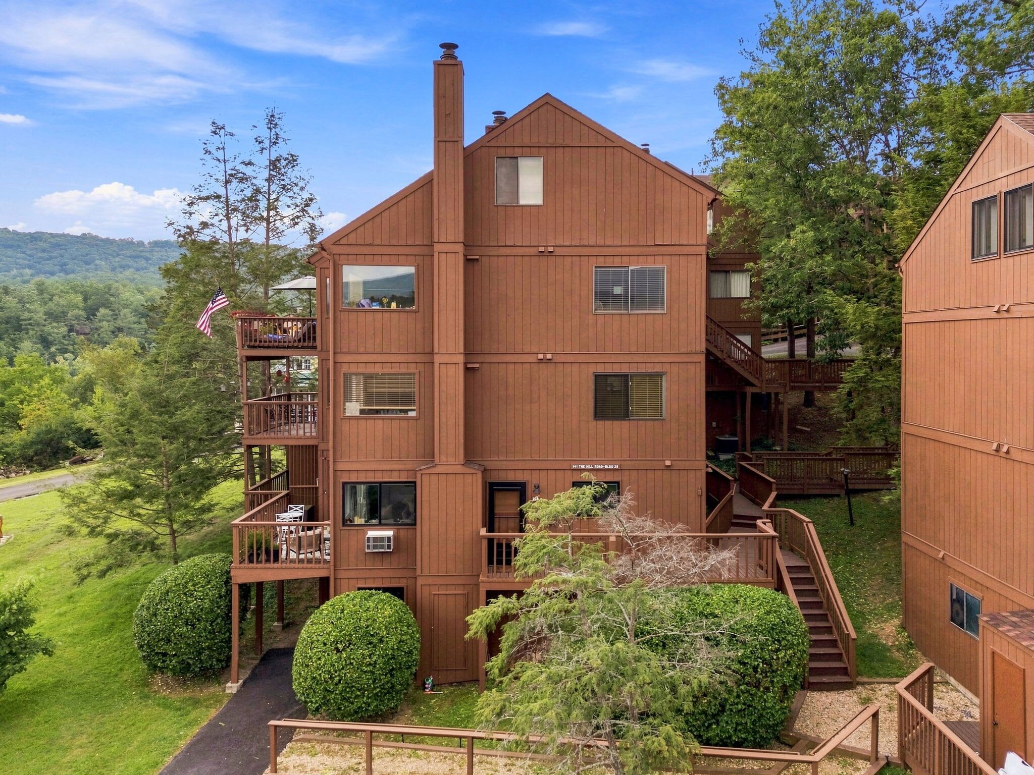 A multi-story wooden building with balconies, a chimney, and a view of the surrounding greenery.
