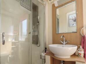 A bathroom with a glass shower enclosure, a white sink with a single faucet, a mirror with a decorative frame, and a towel rack with a pink towel. - 33 Pendle View (Clitheroe)