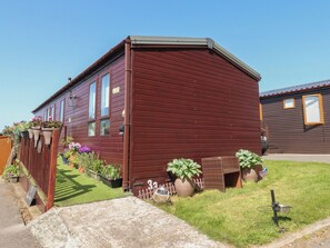A single-story wooden house with a number '33' on the front door, surrounded by a well-maintained lawn and various potted plants. - 33 Pendle View (Clitheroe)