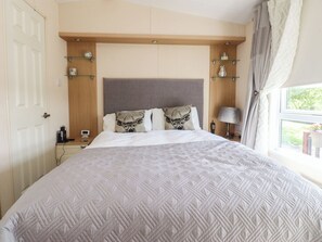 A bedroom with a large bed, a wooden headboard, bedside tables, a lamp, and a window with curtains. - 33 Pendle View (Clitheroe)