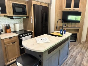 A compact kitchen with a built-in microwave, stove, refrigerator, and a small sink area. - Mountain Hideaway - 2 br 1.5 ba RV (Watauga, TN)