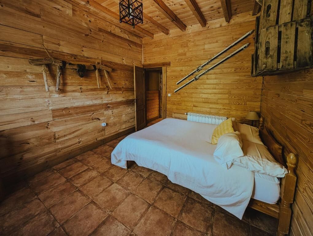 A wooden cabin room with a bed, a door, and a sloped ceiling.