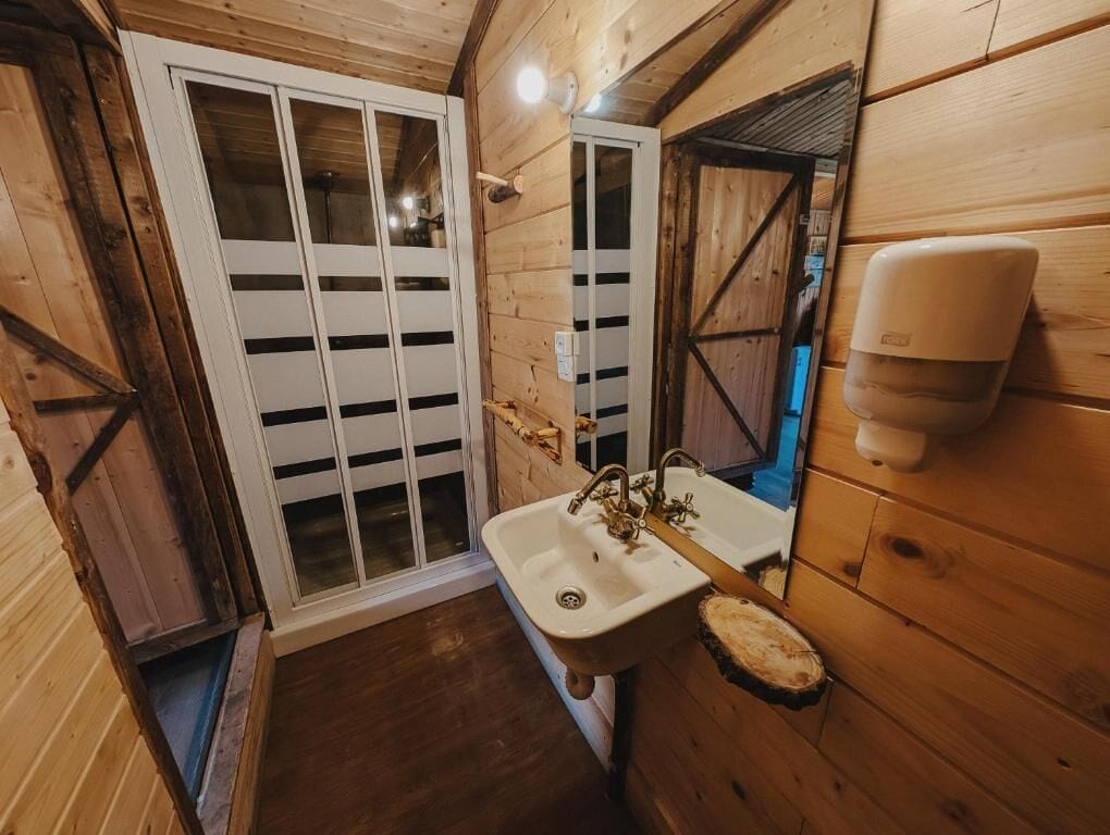 Baño de cabaña de madera con lavabo, espejo y dispensador de jabón.