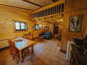 Interior de una cabaña de madera con una mesa de comedor, sillas, un sofá y una zona de cocina.
