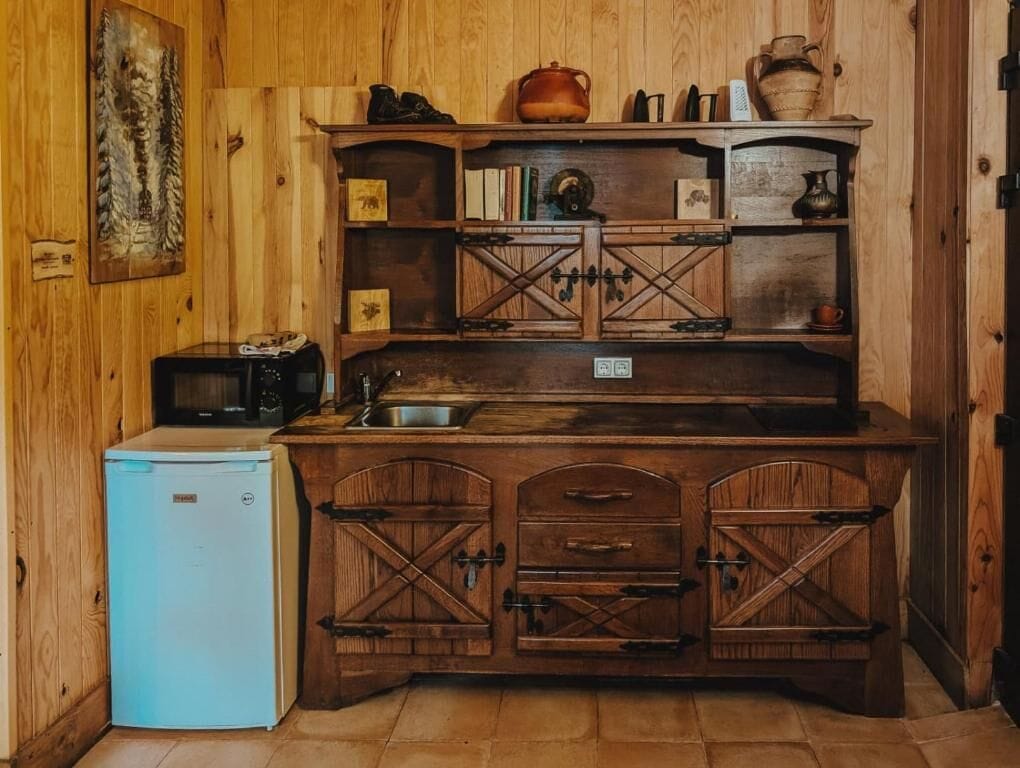 A rustic kitchen with wooden cabinets, a small refrigerator, and a microwave.