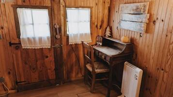 A wooden room with a desk, chair, radiator, and two windows with curtains.